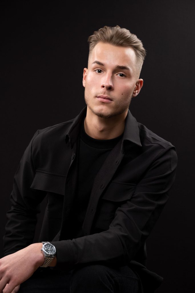 male model in all black clothing in front of black background modelling a luxury watch