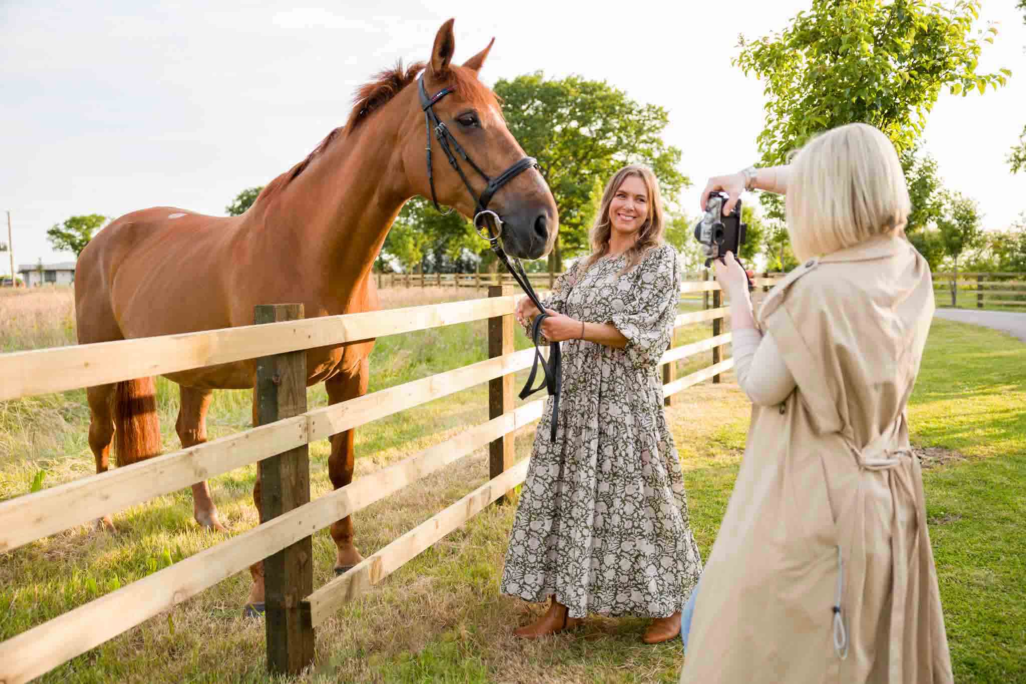 behind the scenes from a fashion photoshoot, a model in a modest dress is posing with a horse